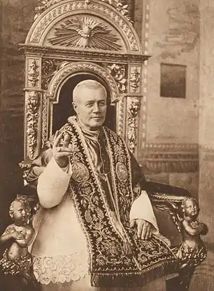 Le Pape, assis sur un trône richement décoré en habits d'apparat avec tiare pontificale et de la main droite donnant une bénédiction. Ornements liturgiques richement brodés.