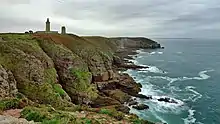 Vue d'une très grande falaise rocheuse. Un phare est visible à son sommet.