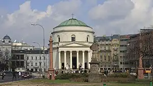 Petit parc avec une statue et un bâtiment blanc entre deux routes.