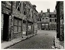 Photographie en noir et blanc d'une rue très dégradée donnant sur une place elle aussi en très mauvais état.