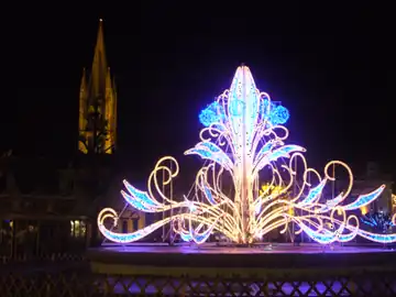 La fontaine illuminée pour les fêtes de fin d'année, avec en arrière-plan l'église Saint-Pierre-du-Queyroix