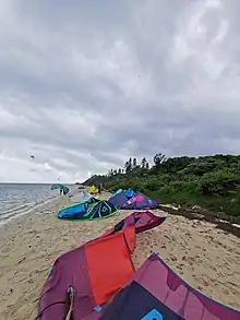 Ailes de kitesurf reposant sur le sable de la plage est de l'îlot maître, vue à gauche sur le lagon, à droite sur le végétation de l'îlot