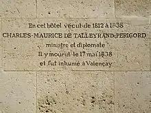 Photo d'un mur de grandes pierres blanches finement jointes, dont une au centre est gravée par les lignes suivantes : « En cet hôtel vécut de 1812 à 1838 / CHARLES-MAURICE DE TALLEYRAND-PERIGORD / ministre et diplomate / Il y mourut le 17 mai 1838 / et fut inhumé à Valençay ».