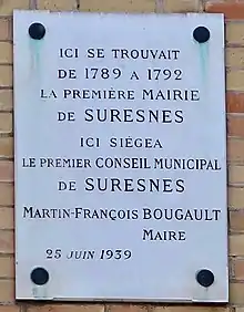 Photographie en couleur d'une plaque posée verticalement sur la façade d'un bâtiment.