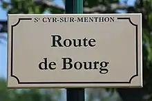 Plaque de rue de couleur blanche où est inscrit Route de Bourg écrit en vert.