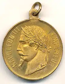 Médaille en bronze dorée représentant le visage de profil de l'Empereur couronné de lauriers ; inscriptions tout autour. Un crochet pour pendre la médaille est fixé sur le dessus de celle-ci.