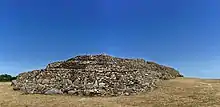 Vue de trois-quarts de l'ensemble du cairn, proue en premier plan. À la proue, on remarque la série de grosses dalles verticales du parement médian.