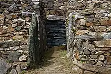 Vue de face. Les parois de l'avant-couloir sont recouvertes de grandes dalles verticales. L'entrée du couloir est murée.