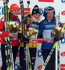 podium avec trois biathlètes, chacune tenant un bouquet dans la main.
