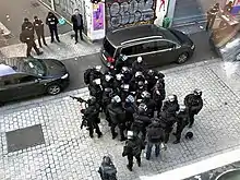 Trois groupes de policiers (un de deux, un de quatre et un de vingt-six) en uniforme avec armes et protection pour la plupart attendent sur la rue de la République.