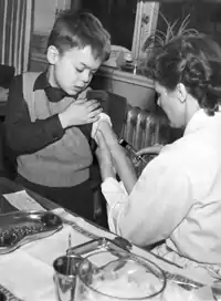 Un garçon, le bras tendu, reçoit un vaccin inoculé par une infirmière.