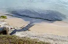 Un rejet d'eau sombre traverse une plage de sable pour venir troubler la mer.