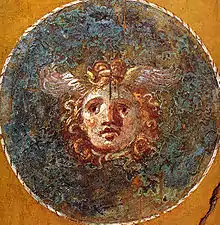 Dans un cercle, masque de Méduse ceint de serpents avec des ailes sur la tête.
