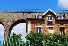 Deux constructions comportant de la pierre meulière, dans le Val-de-Marne : au second plan, à gauche, des arches supérieures des aqueducs d'Arcueil et de Cachan et au premier plan, à droite, une maison particulière, rue du Chemin-de-Fer à Cachan.