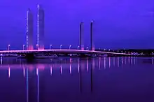 Photographie du pont Jacques Chaban-Delmas de nuit. La nuit est éclairée par le pont, qui reflète des couleurs violettes dans l'eau de la Garonne.
