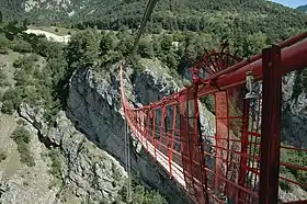 Un étroit pont suspendu peint en rouge passant au dessus d'une profonde gorge.