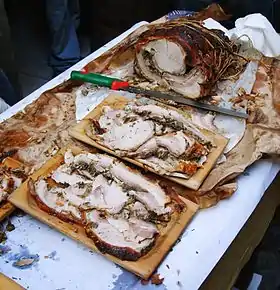 De la porchetta, avec un couteau et deux plats rectangulaires en bois en contenant des tranches