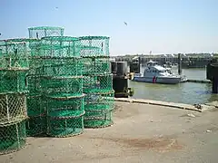 Des casiers de pêche sur un quai du port d'Ouistreham avec, en arrière-plan, la vedette de la Gendarmerie maritime.