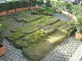 Photographie en couleurs d'un alignement de grands blocs de pierre dans une cour pavée.