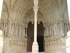 Photographie en couleurs du portail d'une église surmonté d'un tympan en ogive, colonne au premier plan.
