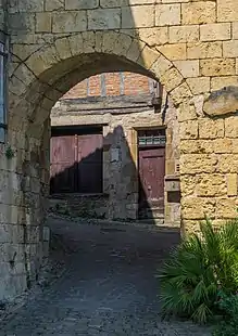 Photo couleur d'une porte voutée au travers de laquelle on voit une maison à colombages et une rue pavée en forte montée.