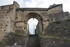 Vue d'une porte romane dans un rempart. Des escaliers traversent la porte.