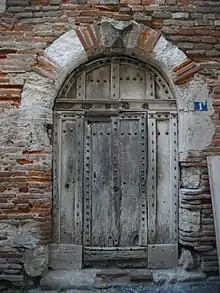 Vieille porte en bois cloutée. Encadrement alternant la brique, la pierre calcaire et le grès rose sur le seuil.