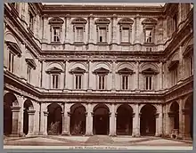 Image en noir et blanc d'une portique sur trois niveaux avec des arcades, puis une série de fenêtres sur le deuxième et troisième niveau séparés par une épaisse corniche.