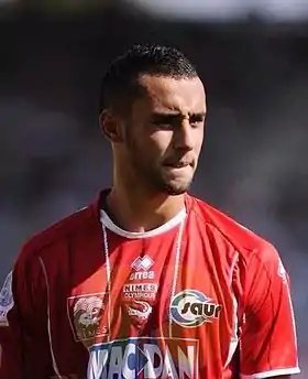 Photographie en couleur d'un homme vu de face en tenue rouge de footballeur.