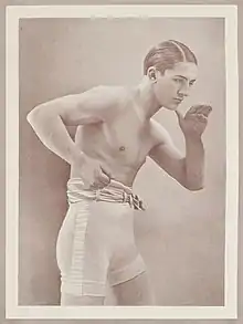 Portrait en noir et blanc d'un boxeur en garde, légèrement penché vers l'avant, sans gant, son poing droit fermé et sa main gauche ouverte.
