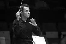 Photographie en noir et blanc d'un homme agitant une baguette de chef d'orchestre.