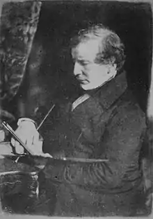 photo en noir et blanc d'un homme en costume occupé à peindre, une palette à la main