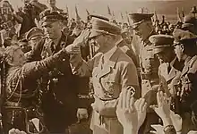 Photographie sépia d'Adolf Hitler, à droite, qu'une femme à gauche tente de toucher de son bras.