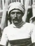 Photo en noir et blanc d'un homme moustachu en polo, un bonnet sur la tête.