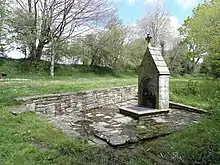 Petite fontaine dont la niche est fermée par une grille. Fleurs à l'intérieur. Le pignon est amorti par une croix.