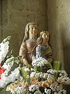 Dans un angle, entourés de fleurs. La Vierge, qui porte une couronne dorée, tient l'enfant dans ses bras.