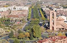 Photographie aérienne d'une avenue bordée d'arbres à la droite figure une église.