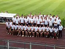 Une quarantaine de joueurs vêtus de t-shirts blancs posent sur une estrade pour une photo de groupe.