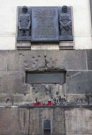 Mur de l'église Saints-Cyrille-et-Méthode de Prague, portant des impacts de balles. Au-dessus, une plaque commémorant le sacrifice des résistants et des prêtres.