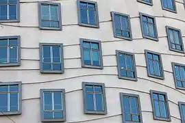 Vue sur la façade de béton d'un immeuble et ses nombreuses fenêtres en décalage les unes des autres et reliées aléatoirement, d'étages en étages, par des lignes courbes.
