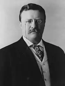Portrait en noir et blanc d'un homme moustachu portant un costume et des lunettes