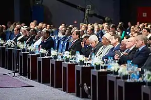Photographie couleur d'une conférence rassemblant de nombreux délégués, essentiellement masculins.