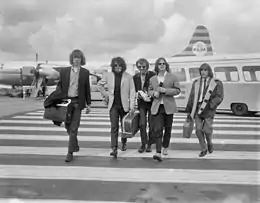 Photo en noir et blanc de cinq jeunes hommes aux cheveux longs dans un aéroport