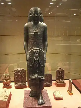 Statue d'individu tenant une statue de guérison d'Horus cippus