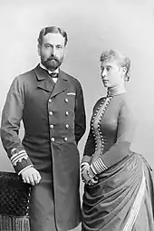 Photographie noir et blanc montrant un homme barbu en uniforme de marin et une femme portant une robe vue de trois-quarts.