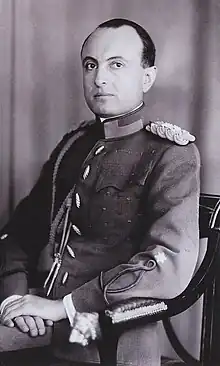 Photographie en noir et blanc montrant un homme assis, de trois-quart, portant un uniforme militaire.