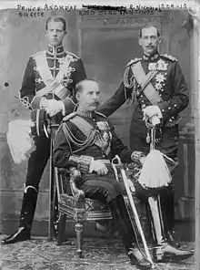 Photographie en noir et blanc montrant trois hommes en uniforme militaire. Celui du milieu est assis et de trois-quart, les deux autres sont debout et de face.
