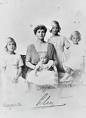 Photographie en noir et blanc d'une femme portant un diadème, entourée de trois petites filles et tenant sur ses genoux un bébé.