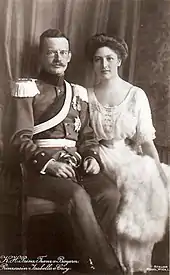 Un couple pose assis : à gauche un militaire et à droite une dame en tenue de cour.