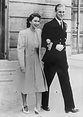 Photographie en noir et blanc d'un couple : la femme porte une robe claire, l'homme a un uniforme de couleur sombre.